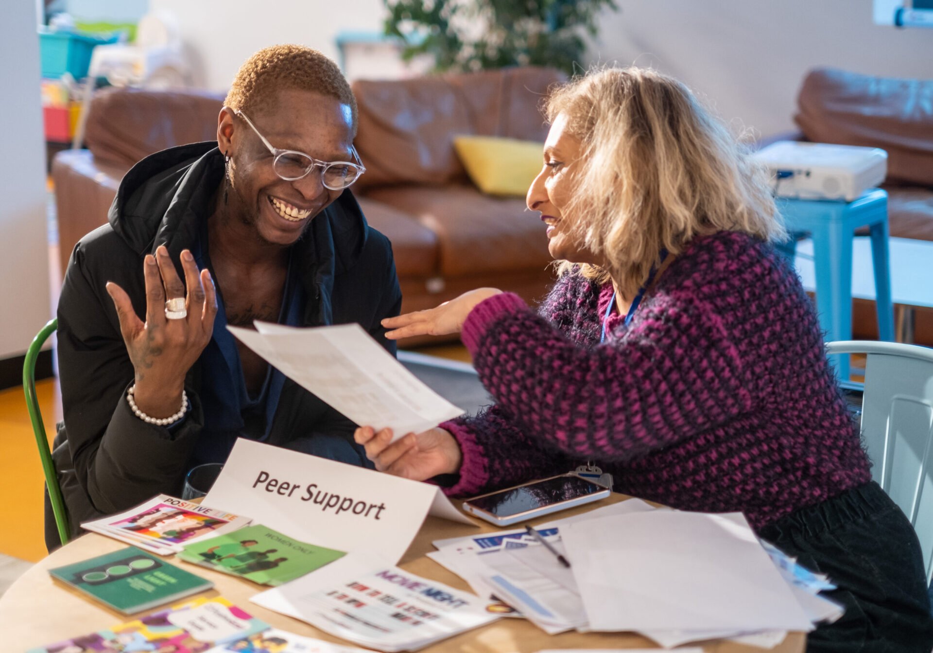 Two women sit at a table smiling holding paperwork