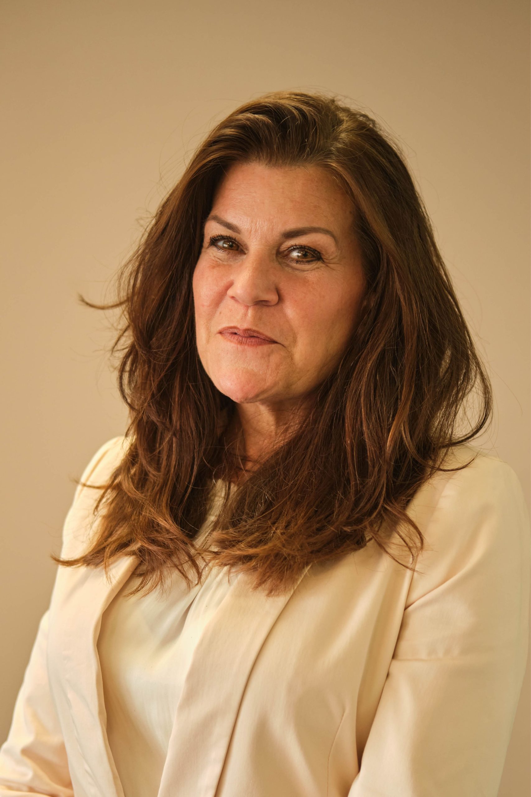 The image shows a person with long brown hair, wearing a light-colored top. The background is a neutral color.