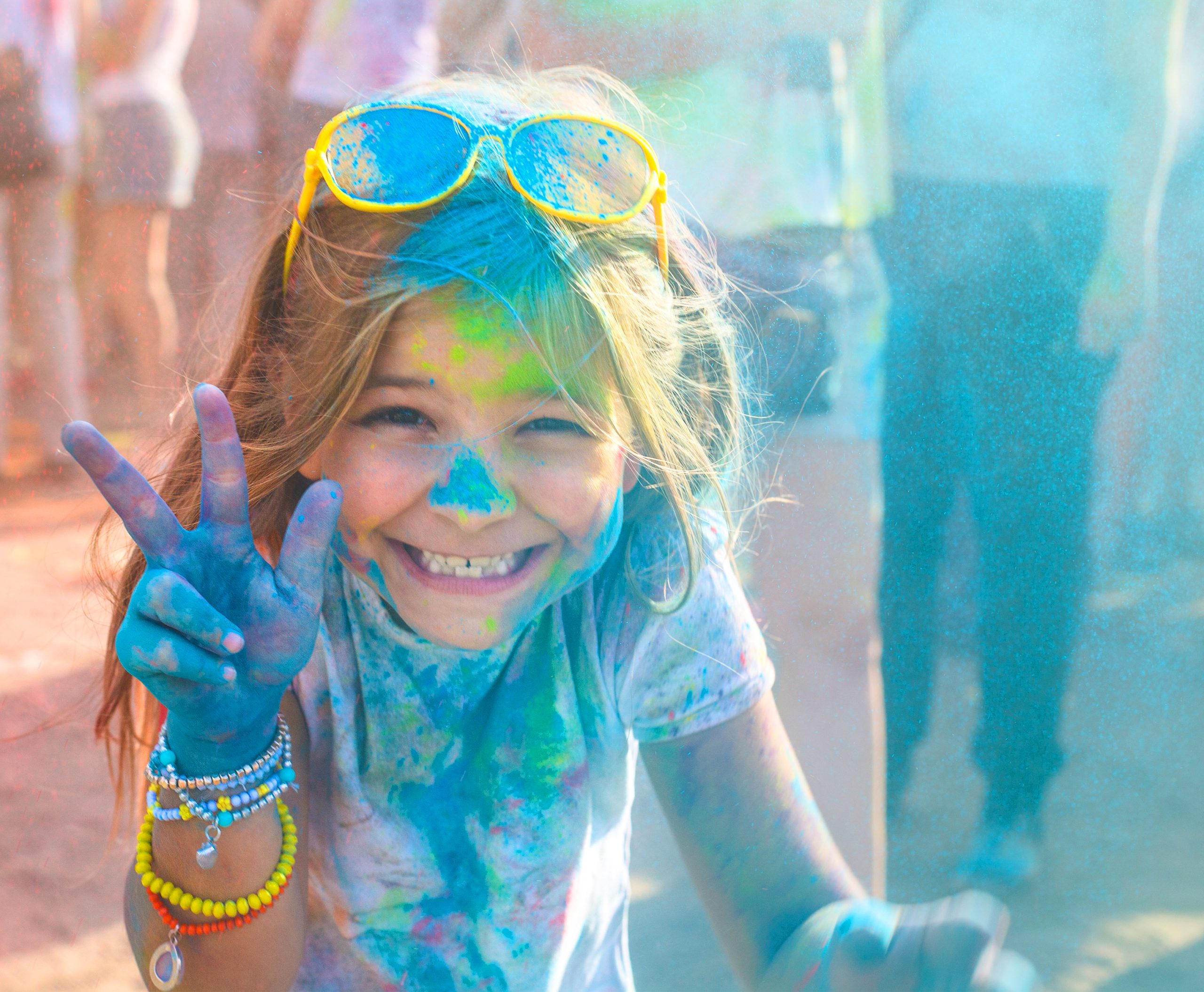 The image shows two smiling people covered in colorful powders, likely participating in a celebration similar to Holi, a festival known for throwing and applying bright colors. There's a festive atmosphere with vibrant colors on their faces and clothes.
