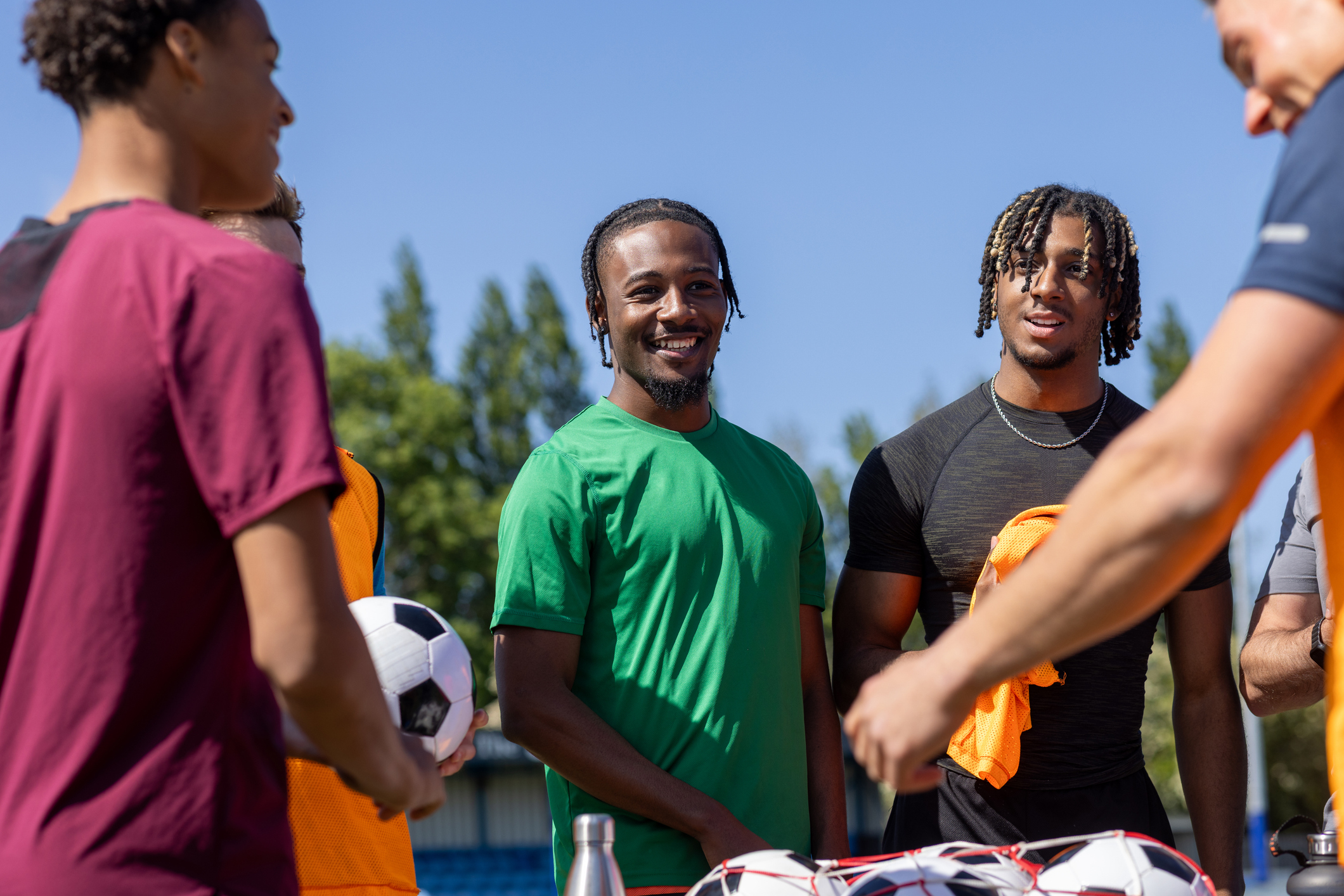 A group of young men stand together outdoors with footballs and training bibs.