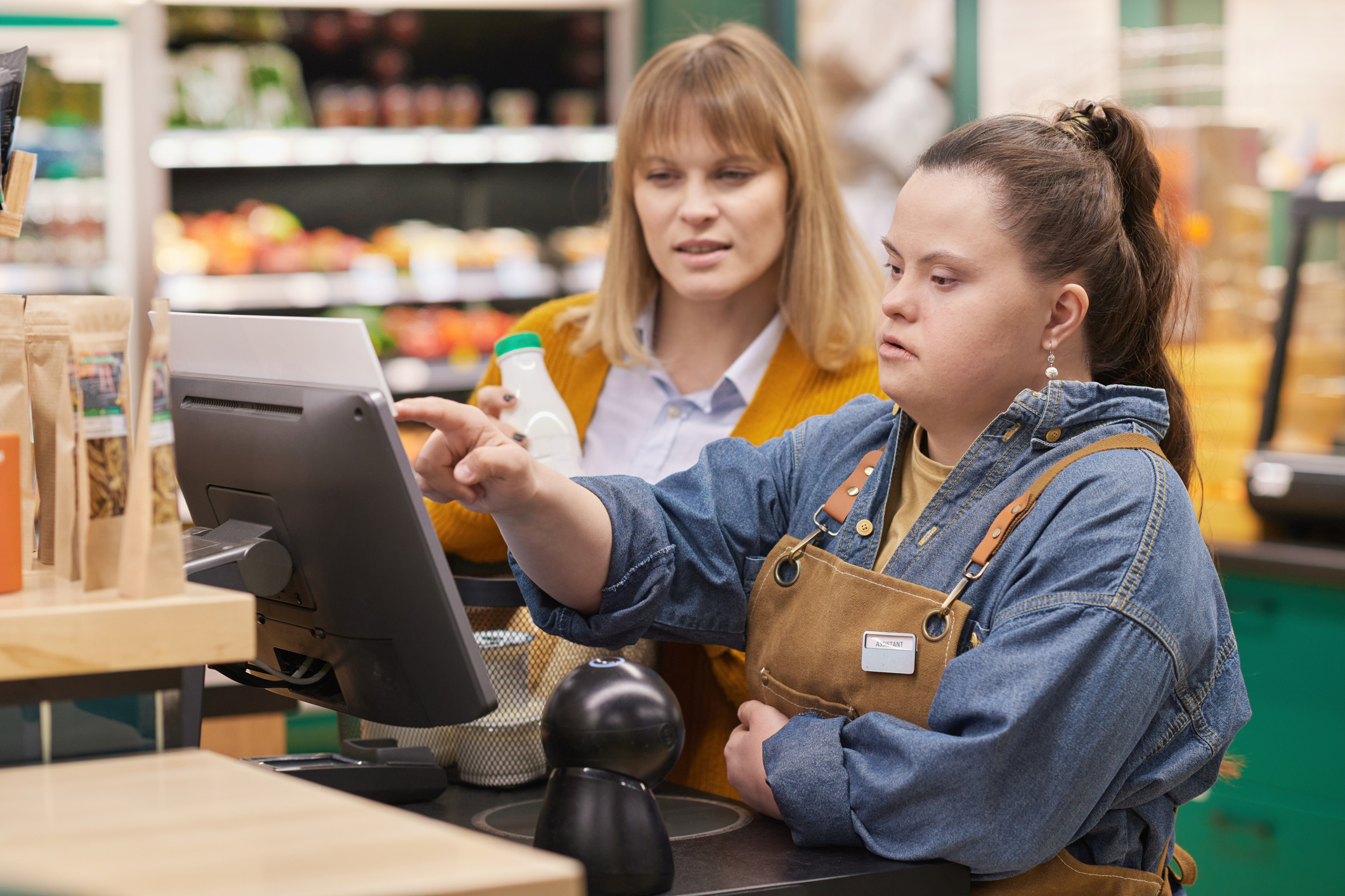 A shop assistant with Down's syndrome points to a checkout screen while helping a customer at a grocery store
